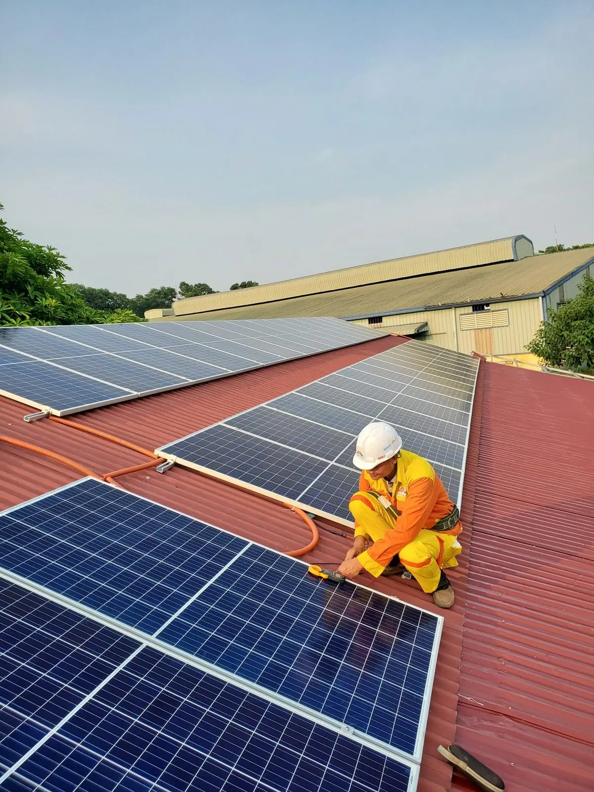 An installer in a hard hat fixing solar panels to a red metal roof