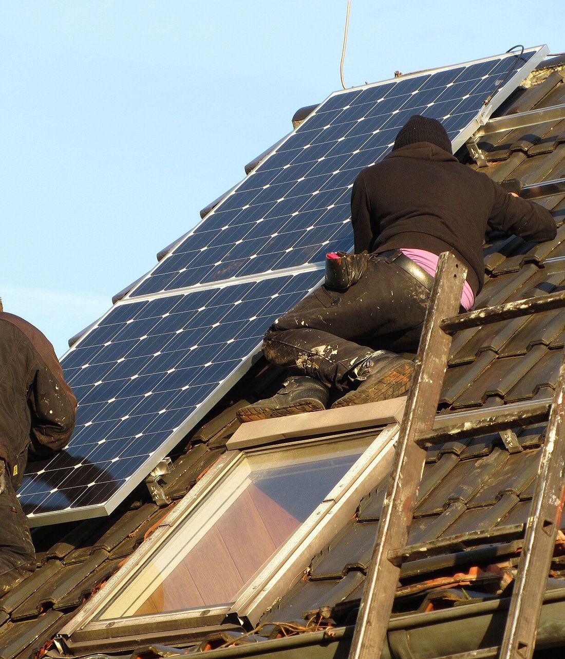 Two installers mounting monocrystalline solar panels on a residential tile roof