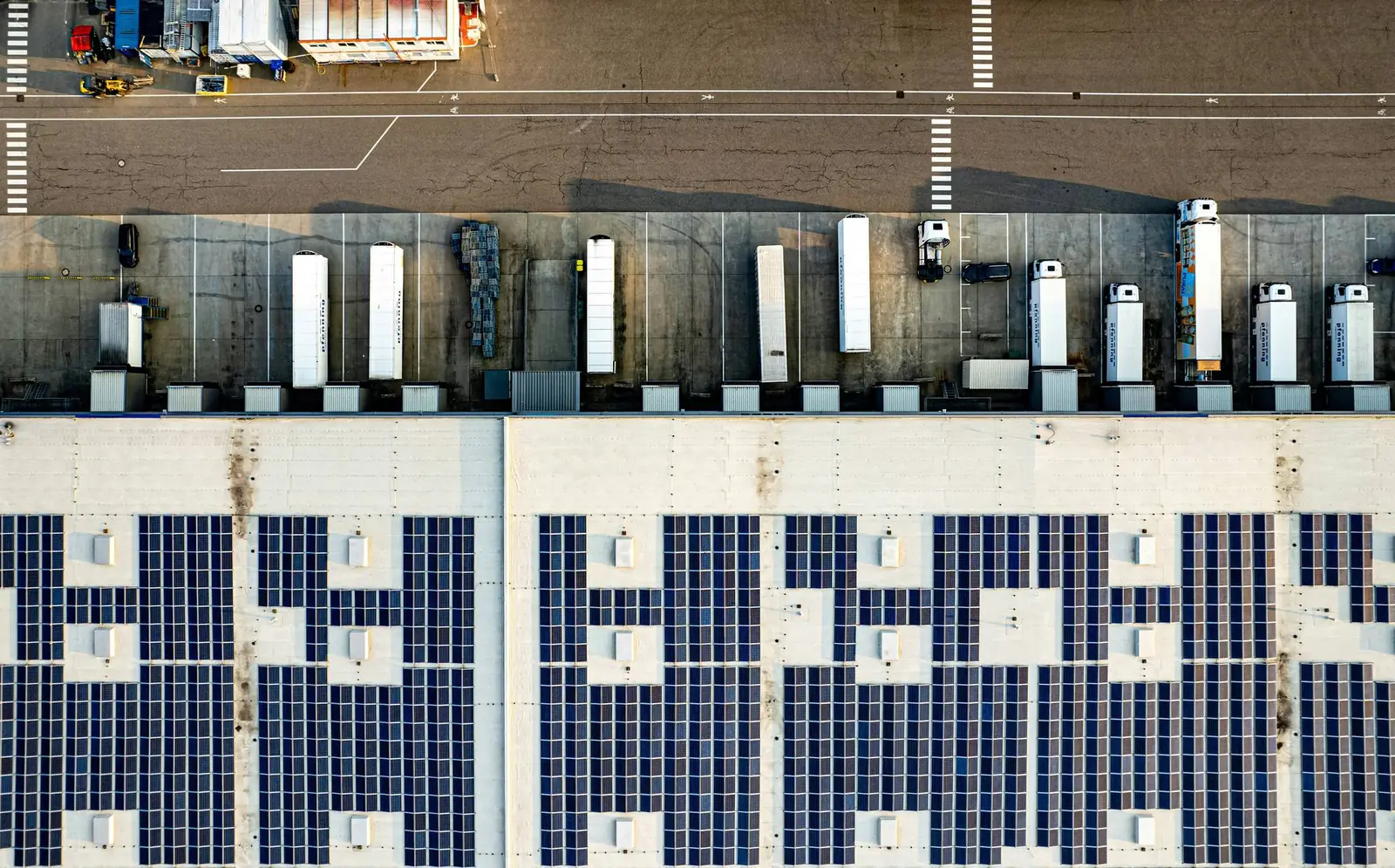 Aerial view of a logistics warehouse with its roof covered in solar panels and trucks at the loading docks